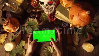 一个男人在智能手机上玩游戏，在万圣节的场景背景下用绿色屏幕玩游戏